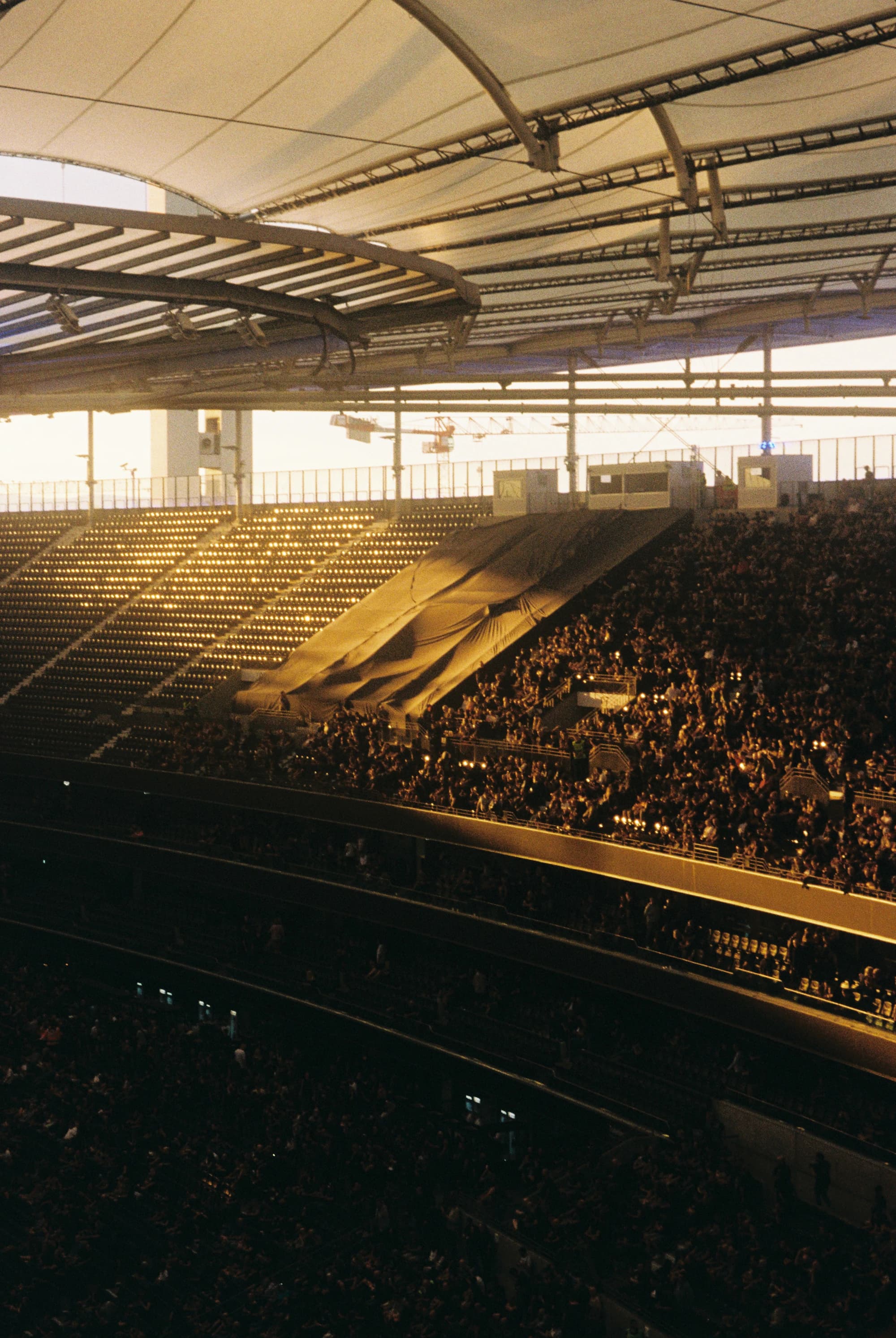 Supporters gathering beneath a stadium roof at sunset.