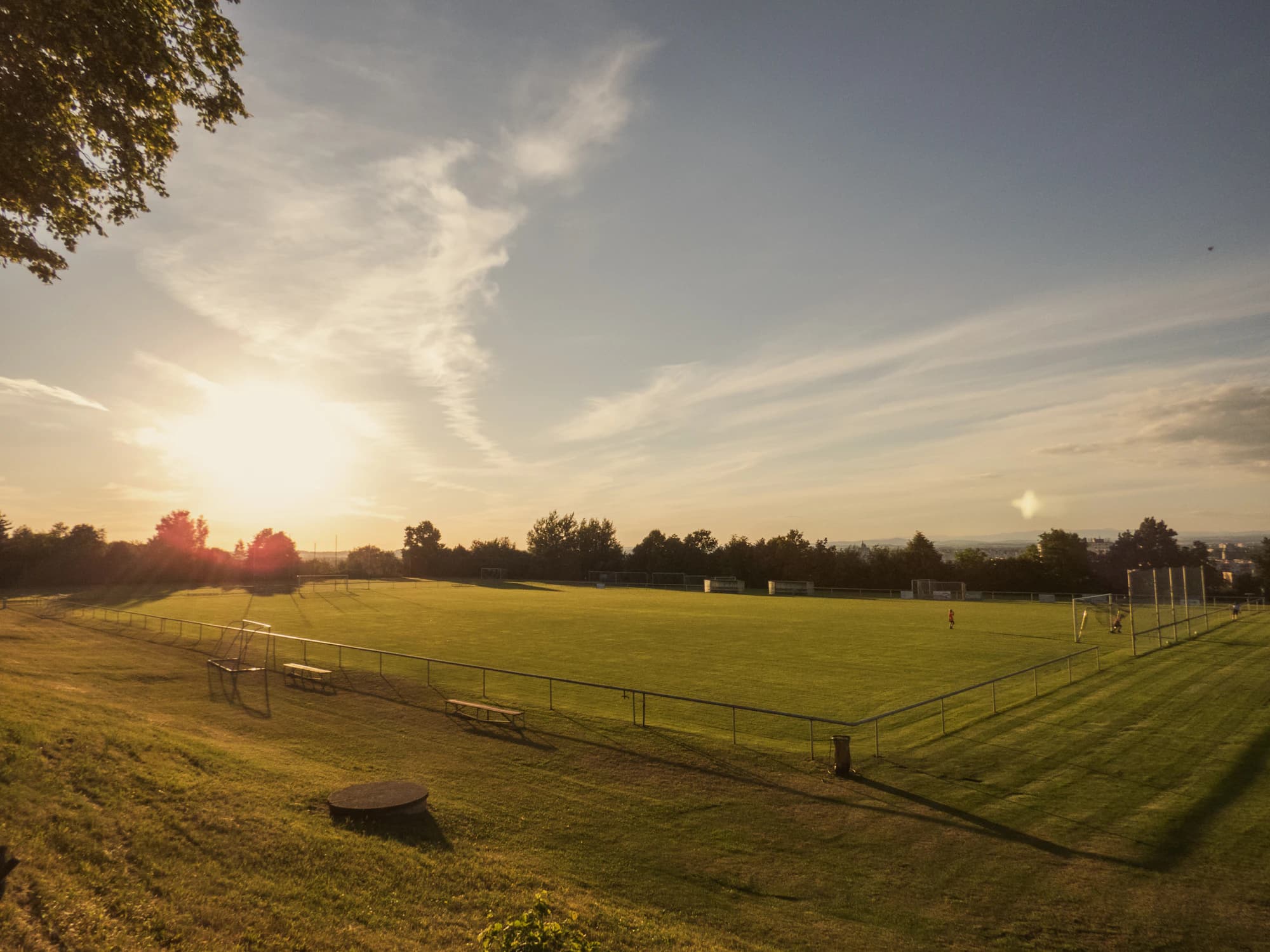 A community football pitch at sunset, framed by trees.