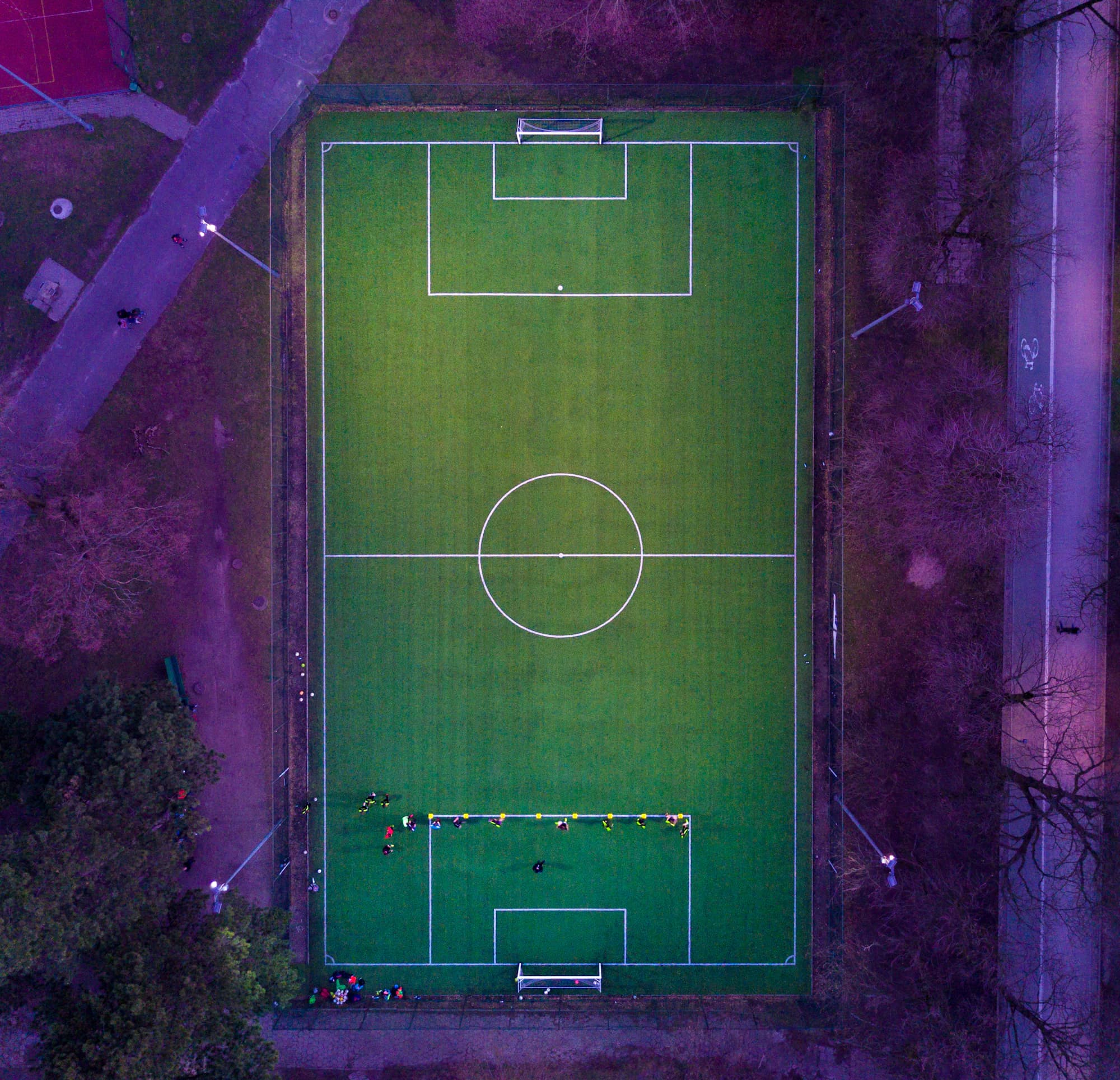 A football pitch viewed from above, framed by trees and evening light.
