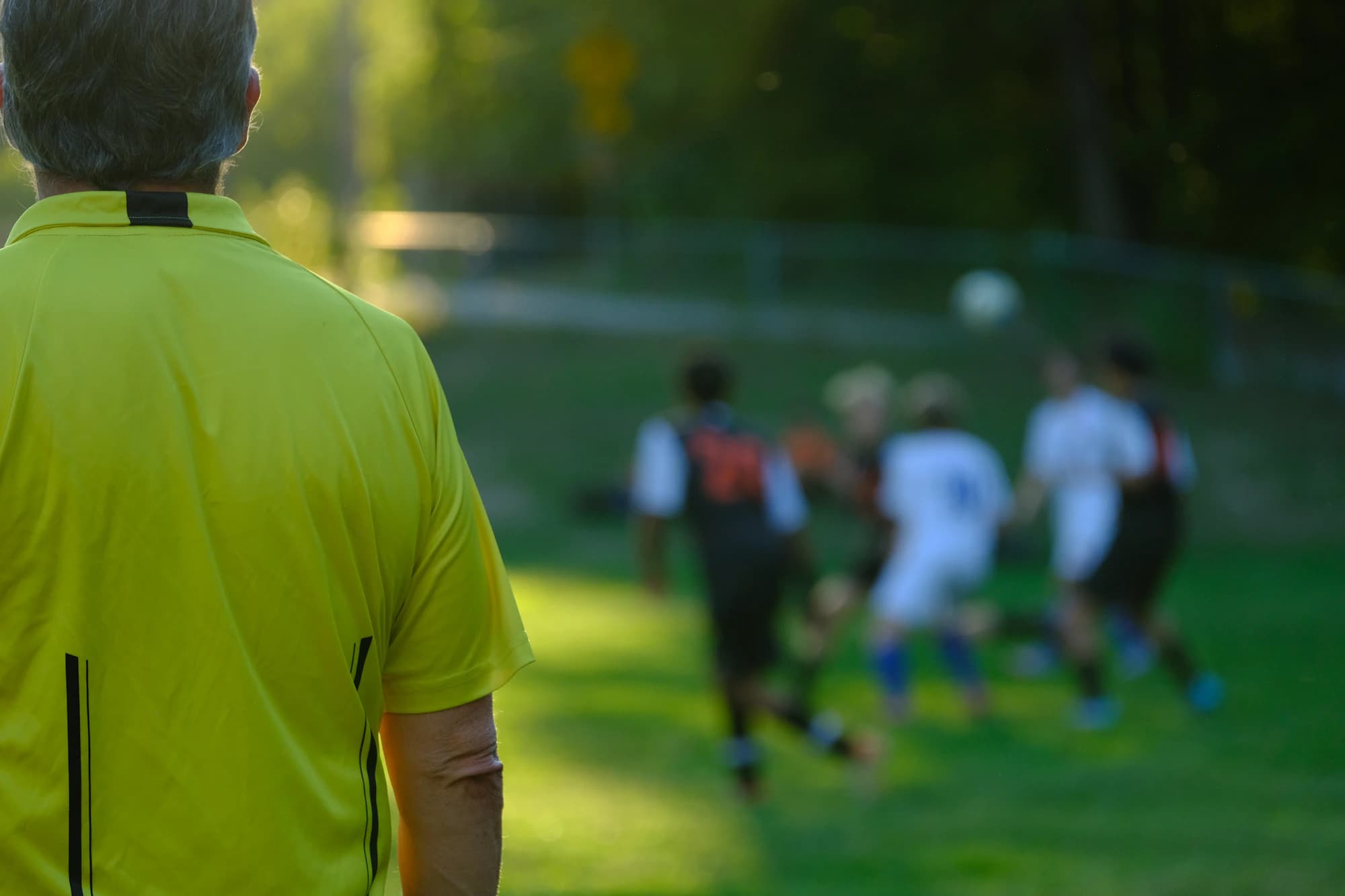 A referee observing a football match in golden afternoon light.